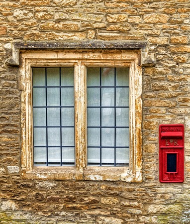 An old red postbox next to a house window in an English village.の写真素材