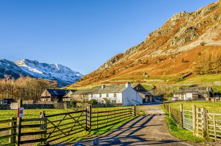 Typical whitewashed farm house and barn with track leading to it at Langdale in the English Lake District, Cumbria. Snow covered fell beyond, background of cloudless blue sky.の写真素材