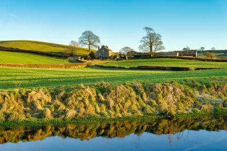 A view of the Lancaster canal with a farm house, bordered by two treesの写真素材