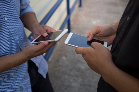 Mockup image of white mobile phone with blank black screen.Two young man are searching needed information for work in internet via cell telephones.の写真素材
