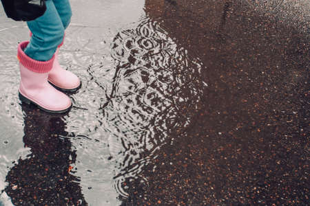 Child wearing pink rain boots and jumping into a puddle.の写真素材