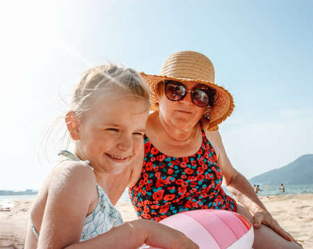 Happy grandmother and granddaughter are resting on the beach near the seaの写真素材
