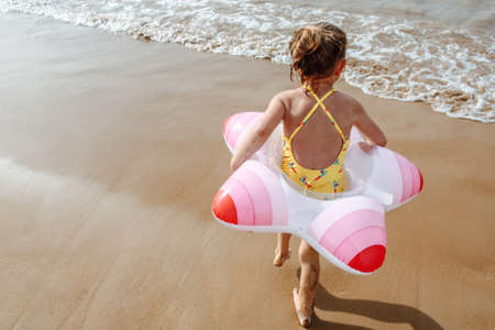 Happy little girl child with inflatable circle and having fun on the beach