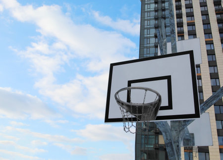 Street basketball hoop, net and board against the background of the blue sky and clouds and urban...