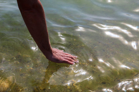 Close-up photo of a man's hand gently touching the surface of the sea water, capturing connection with nature and calm emotions.の写真素材