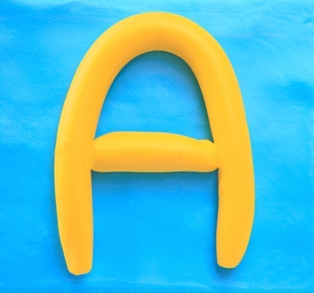 yellow clay alphabet letter with drop shadow on blue clayの写真素材