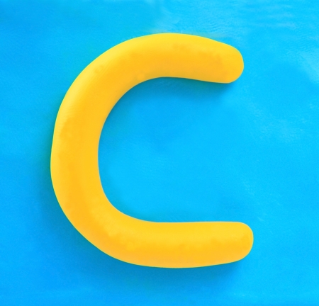 yellow clay alphabet letter with drop shadow on blue clayの写真素材