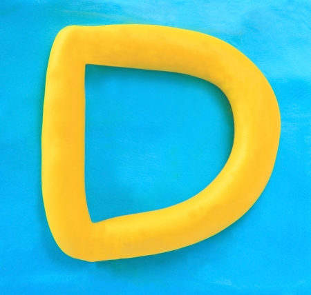 yellow clay alphabet letter with drop shadow on blue clayの写真素材