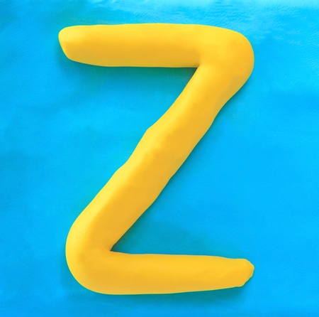 yellow clay alphabet letter with drop shadow on blue clayの写真素材