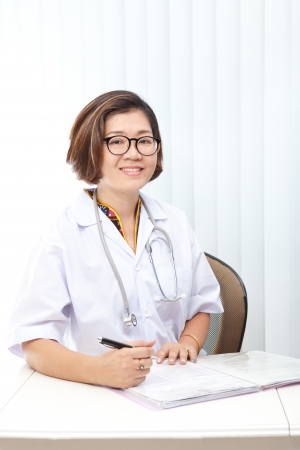 female doctor sitting in working room and writing on reportの写真素材