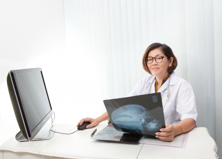 doctor sitting in working room and reading data from head skull x-ray and working on computerの写真素材