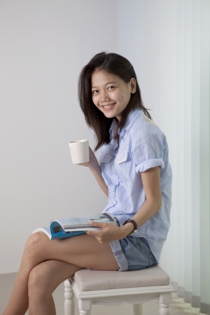 asian woman and coffee cup sitting in living roomの写真素材