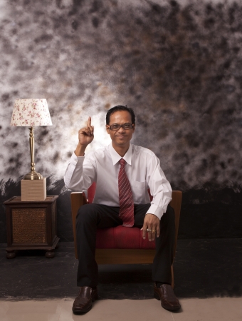 young man in white shirt sitting on red sofa pointing to aboveの写真素材