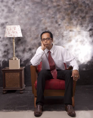 business man sitting on wood sofa with serious face use for multipurposeの写真素材