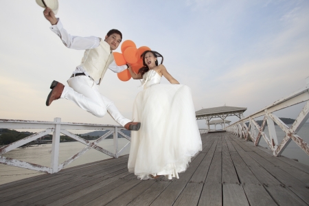 couple of groom and bride  in wedding suit  jumping with glad emotion on wood bridge  use for wedding and honey moon ceremony themeの写真素材