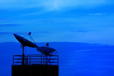 	satellite dish obove building roof with dramatic blue skyの写真素材