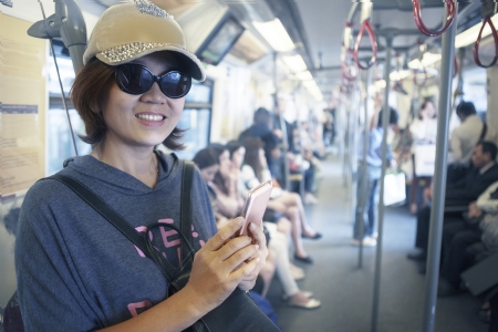 face of woman in sky train with smart phone in hand use for city life and traveling themeのeditorial素材