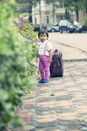 children standing with big suitcase on road sideの写真素材