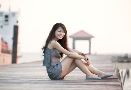 beautiful asian woman sitting on wood pier with relaxing emotion and smiling to camera use for attractive woaman and people female topic の写真素材