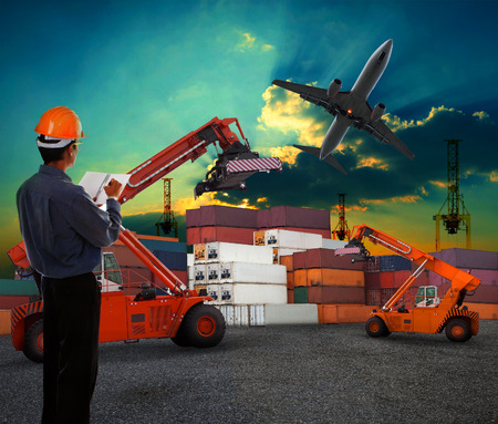 working man in logistic business working in container shipping yard with dusky sky and jet plane cargo flying above use for land to air transport and freightの写真素材