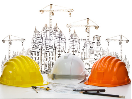 safety helmet on engineer working table against sketching of building construction and high crane の写真素材