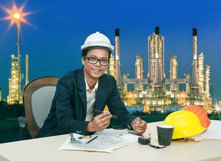 engineering man working on table aginst beautifult lighting of oil refinery plantの写真素材
