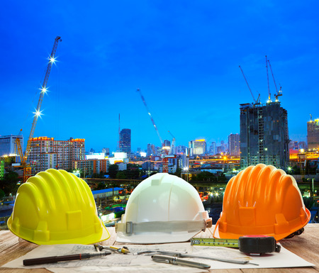 engineer working table with hard hat plan and writing tool against beautiful lighting and urban...