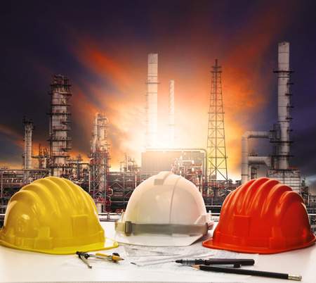 safety helmet and working sheet on engineer working table with oil refinery background