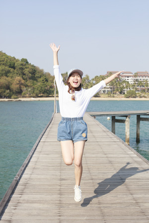 portrait of young beautiful woman jumping with happy emotion on wood piers at sea side use for people activities in holiday vacationの写真素材