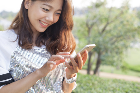 beautiful woman playing and touching on smart phone screen in outdoor of home garden fieldの写真素材