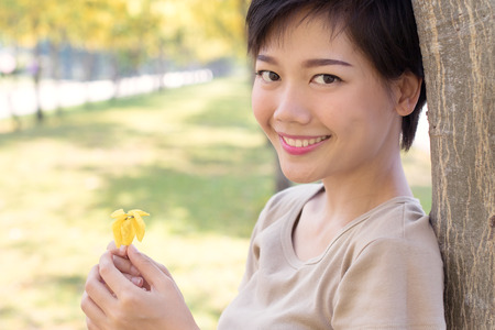 close up face of young asian woman with smiling face and relaxing emotion standing in yellow blooming flowers park use for people healthy life and beauty health careの写真素材