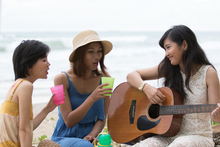 portrait of asian woman and friends group playing guitar and happiness singing a song use for people relaxing holiday at sea sideの写真素材
