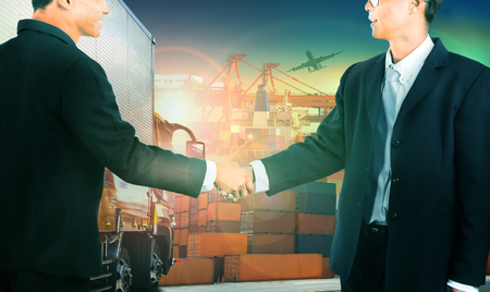 two business man shaking hand against container truck in shipping port ,container dock and freight cargo plane flying above use for transportation and logistic indutryの写真素材
