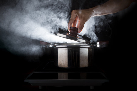 hand of chef open hot stream pot with beautiful studio lighting against black background use for people cooking food and water boiled in kitchen roomの写真素材