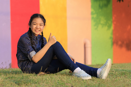 asian girl relaxing sitting on green grass field of public park and hand sign ok ,all right with toothy smiling face happiness emotionの写真素材