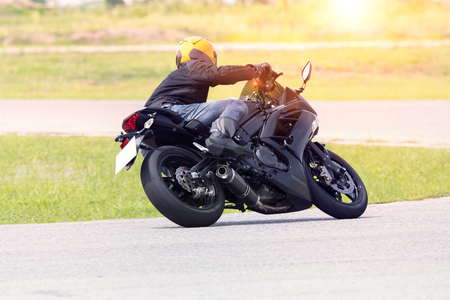 young man riding motorcycle in asphalt road curve wearing full safety suitの写真素材