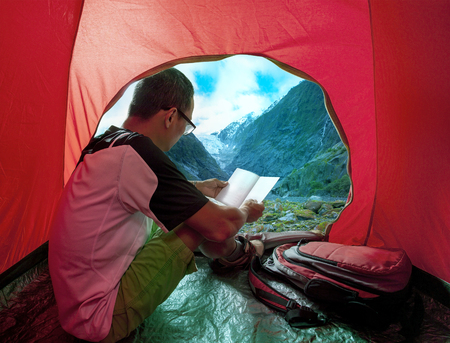 camping man reading a traveling guild book in camp tent beautiful mountain scenicの写真素材