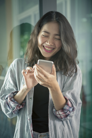 asian younger woman laughing with happiness emotion looking and reading chat message  on smart phoneの写真素材