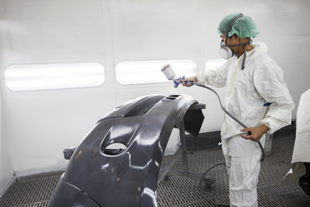 worker man spray painting on car body part in car maintenance service paint roomの写真素材