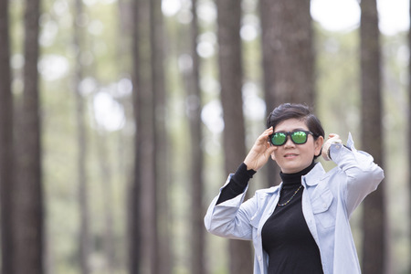 asian woman wearing sun glasses standing in pine wood forest relaxing emotionの写真素材