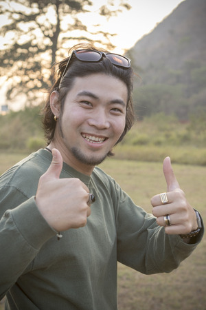 portrait of asian hipster man toothy smiling face with happiness emotion and feeling good with hand signの写真素材