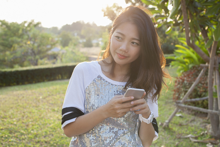 asian younger woman with smartphone in hand happiness thinking ,relaxing outdoorの写真素材