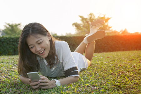 asian younger woman lying on field playing smart phone and laughingの写真素材