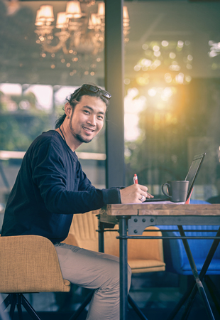 asian younger freelance man working at home office  with computer laptop toothy smiling faceの写真素材
