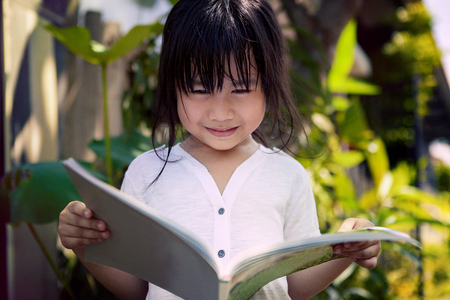 asian children reading a book in home gardenの写真素材