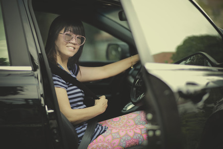 younger woman sitting on driver seat of suv car and fasten seat belt