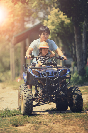 father and daughter riding on quad atv on dirt fieldの写真素材