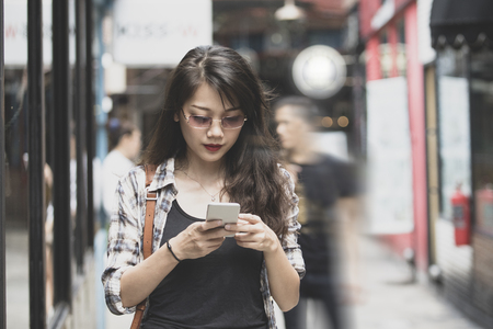 beautiful asian woman walking on urban street and  connecting on smart phoneの写真素材