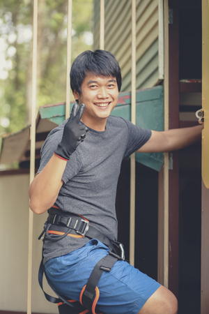 asian younger man wearing safety harness suit preparing to hiking artificial cliff in adventure baseの写真素材