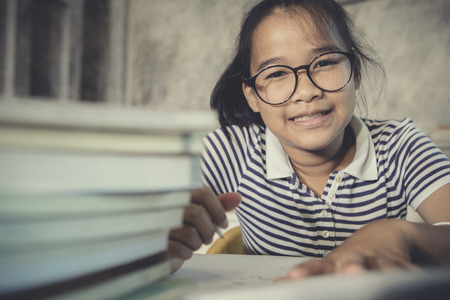 asian teenager wearing eye glasses doing home work with stack of school book foregroundの写真素材